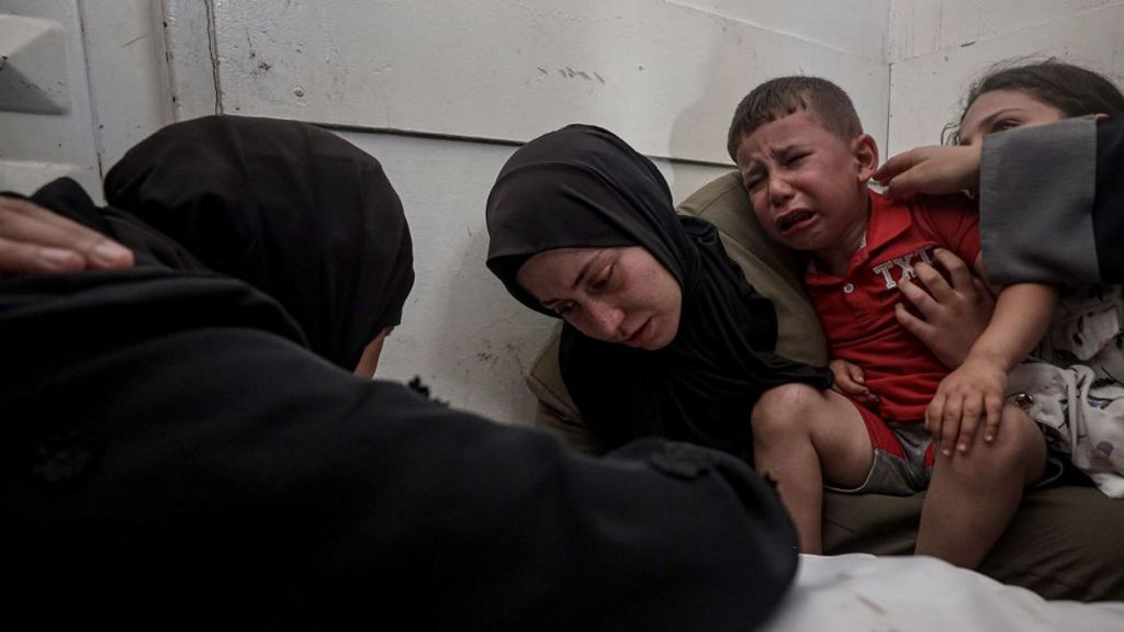 women and a child mourn over a dead body (not shown)