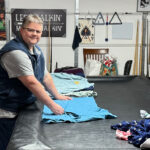 Melia Long folding laundry on a pool table in her garage, surrounded by clothing and household items